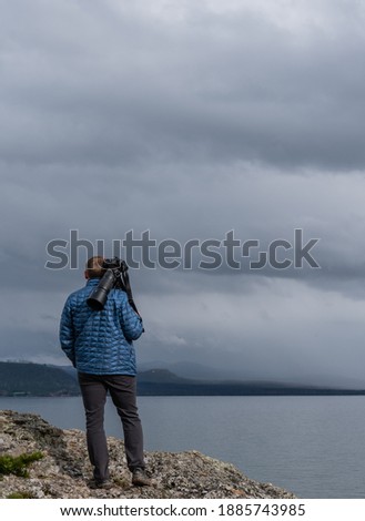 Man Carries Large Lens Over Back at shore of Yellowstone Lake