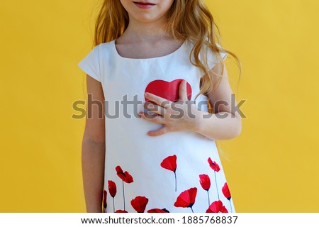 little girl presses a red paper heart to her chest. Health and Valentine's day concept