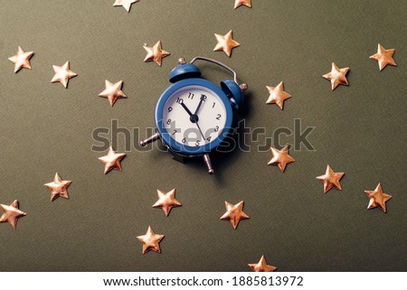 A close up picture of a litlle blue clock between a lot of stars on a dark table
