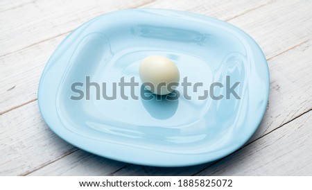 Only one boiled egg on a blue plate on a white wooden background.