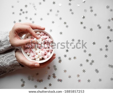white cup with marshmallows on a white background with silver snowflakes.