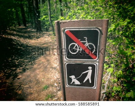 A filtered photo of a sign post with symbols for biking not allowed and dog walking on leash allowed.