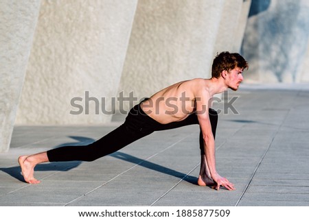 Young red-haired male athlete performing stretching after training to gain flexibility and relax his muscles, outdoors with unfocused background.