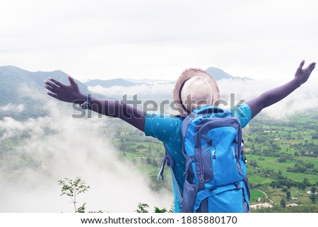 Freedom african  male traveler and hiker with backpack at the top of the hill covered with mist.