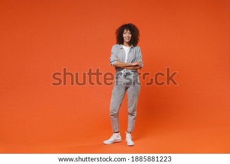 Full body length smiling young african american stylish woman 20s in gray casual clothes posing standing isolated on orange background studio portrait. Mock up copy space. Holding hands crossed folded Royalty-Free Stock Photo #1885881223
