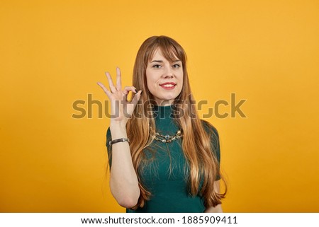 View of hand fingers showing ok sign, gesturing making okay, human emotions, facial expressions, feelings. Young attractive woman, dressed green shirt blonde hair, yellow background