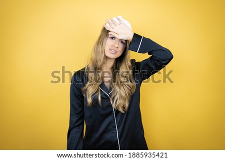 Young pretty woman wearing sleep mask and pajamas over isolated yellow background ouching forehead for illness and fever, flu and cold, virus sick
