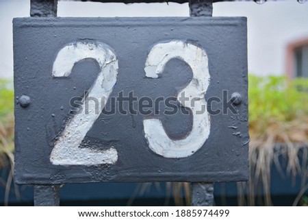A blue house number plaque, showing the number twenty three (23)
