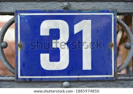A blue house number plaque, showing the number thirty one (31)