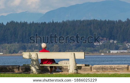 An old woman rests in a park bench by the sea on a sunny autumn day. Selective focus, street view, travel photo.