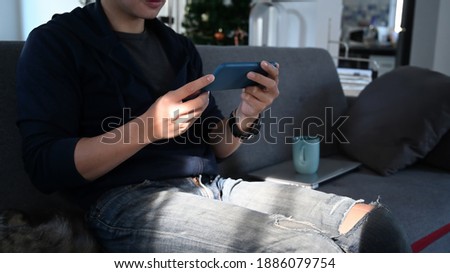 Cropped shot man looking at his smartphone and sitting at sofa.