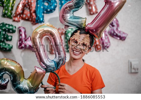 Cute young girl with a smile in a festive outfit on studio background holding colorful balloons from 2021 numbers
