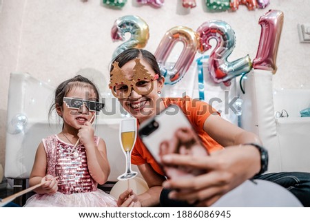 Cute young girl and little girl with a smile in a festive outfit on studio background holding colorful balloons from 2021 numbers