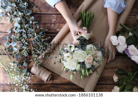 Florist wrapping beautiful wedding bouquet with paper at wooden table, top view Royalty-Free Stock Photo #1886101138