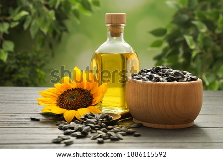 Sunflower, bottle of oil and seeds on wooden table against blurred background