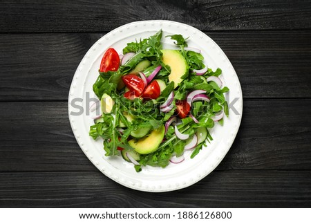 Delicious salad with avocado, arugula and tomatoes on black wooden table, top view