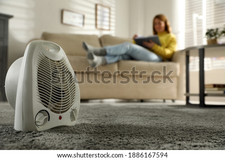 Woman reading book in living room, focus on electric fan heater Royalty-Free Stock Photo #1886167594