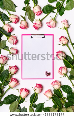 Floral composition. Frame made of beautiful pink roses flowers with clipboard on white background. Mock up for greeting card. Happy women's or mother's day concept. Flat lay, top view, copy space