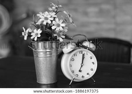 Black and white picture of some grass flowers in a cup and a clock on blur background