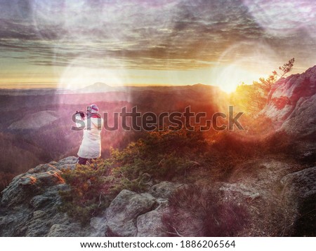 Female outdoor adventure photographer is seen from behind. She photographs fall landscape. Copy space. Abstract filter.