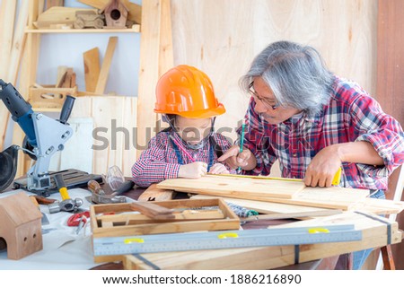 Happy carpenter family. The little girl and her grandfather smiled happily while working on woodwork in a wooden shop.