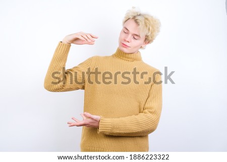 Young handsome Caucasian blond man standing against white background gesturing with hands showing big and large size sign, measure symbol.