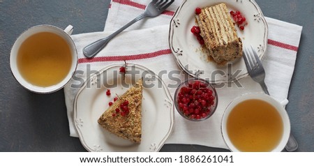 Food background. Two pieces of honey puff cake with frozen red currant berries with honey and tea on a gray background.