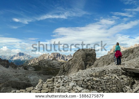 A woman hiking in high and desolated mountains in Italian Dolomites. She stands at the edge of a slope and enjoys the idyllic landscape. Raw and unspoiled landscape. Sunny day. Endless mountain chains