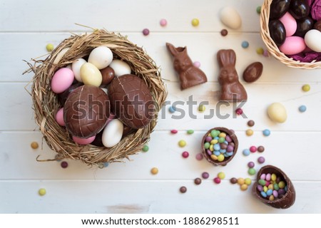 Top view of easter edible eggs on nest, chocolate rabbits and sweets on white wooden table Royalty-Free Stock Photo #1886298511