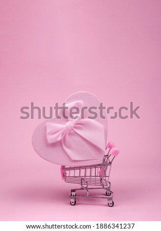 Pink heart gift with bow for Valentine's Day in shopping scart on a pink background, delivery gift