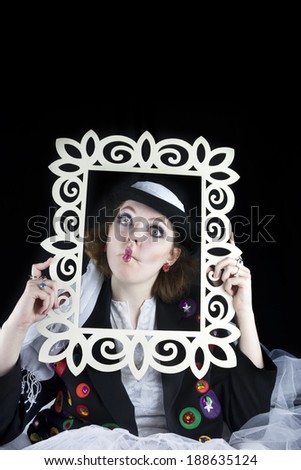 Pretty young woman making funny face and holding picture frame wearing hat and crinoline