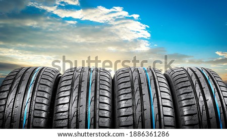 Summer car tires on over blue sky with clouds. Tire stack background. Car tyre protector close up. Black rubber tire. Brand new car tires. Close up black tyre profile. Car tires in a row Royalty-Free Stock Photo #1886361286