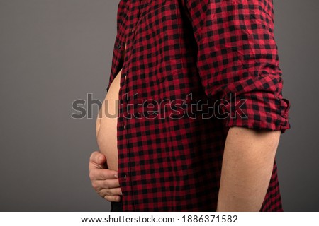 Close up picture of young man's bloated stomach in front of grey background