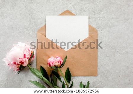 Mockup invitation, blank paper greeting card and peonies on gray stone table. Flower background. Flat lay, top view.