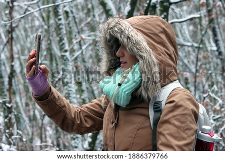 Blonde girl taking picture of forest covered in snow. German winter photography. Girl with winter jacket and cell phone during hike in palatinate forest.