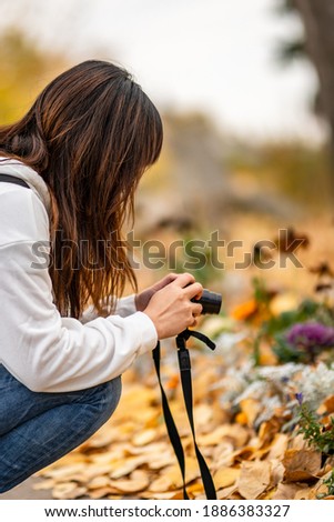 A young girl squatting and taking pictures with a camera in the autumn garden.