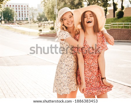 Two young beautiful smiling hipster female in trendy summer sundress.Sexy carefree women posing on the street background in hats. Positive models having fun and hugging Royalty-Free Stock Photo #1886383453