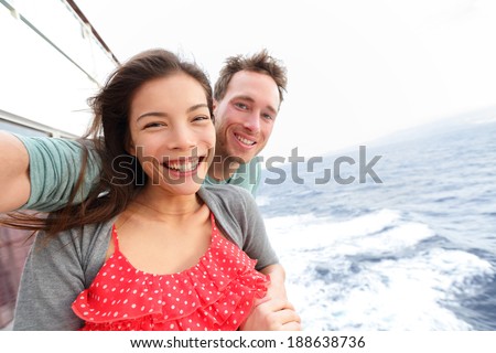 Cruise ship couple taking selfie self portrait photo romantic. Happy lovers, woman and man traveling on vacation travel sailing on open sea ocean enjoying romance. Young Asian woman and Caucasian man.