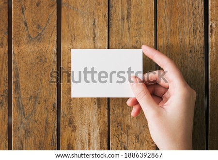 Woman hand hold blank white business card mockup on a wooden table. Logo and branding design template concept