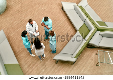 Top view of a team of doctors who stand in the lobby of a modern clinic and discuss methods of treating patients.