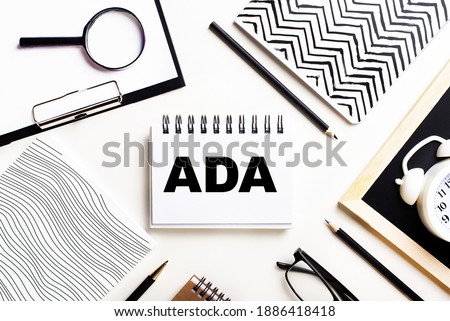 On a light table are notebooks, a magnifying glass, an alarm clock, glasses, and a pen. And in the center is a notebook with the text ADA