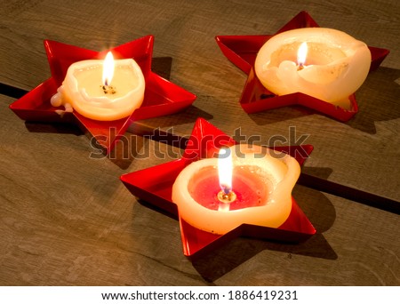 Inside the star-shaped red candle holders, three candles are burning and melted.