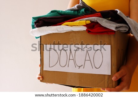 Woman holding a Donation Box full of clothes, with Donation written in Portuguese (Doação).
