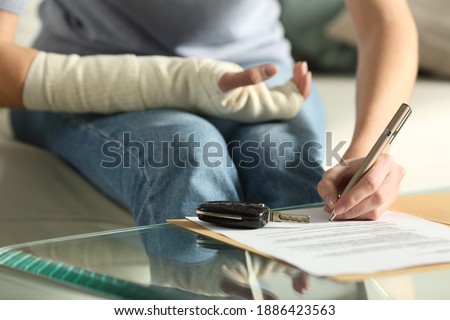 Close up of a lady hands with broken arm signing insurance document after car accident at home