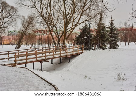 Winter park landscape.The city park is covered with snow. Snow on the wooden sidewalks and bridges of the park is trampled by the walking. The bridges are fenced with wooden railings. 