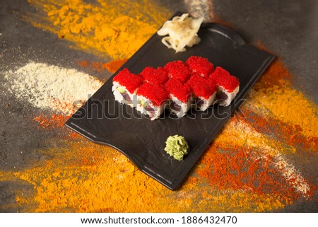 Top view of Japanese seafood sushi roll dish with tuna Maguro, avocado. red flying fish roe Tobiko on top served with wasabi, ginger. turmeric, garlic, curry, paprika spices scattered on background