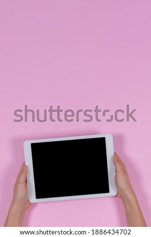 Kid hands holding digital tablet computer on pastel pink background. Top view