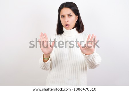 Young brunette woman wearing white knitted sweater against white background Moving away hands palms showing refusal and denial with afraid and disgusting expression. Stop and forbidden.