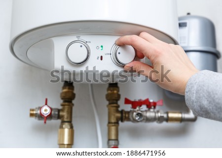 Female hand puts thermostat of electric water heater (boiler) in low low power consumption mode . Household enegry saving equipment Royalty-Free Stock Photo #1886471956
