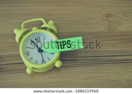 Selective focus of alarm clock and memo note written with text TIPS over wooden background.